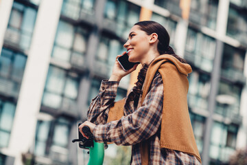 Fototapeta premium Smiling Young Woman Talking on Her Smartphone Outdoors Near Modern Urban Buildings on a Pleasant Day