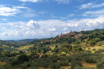 Naklejka premium Panoramic view of rolling hills with olive groves and a picturesque hillside village under a bright blue sky with scattered clouds