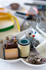 An assortment of colorful sewing and crafting supplies, featuring spools of thread, a needle, pins, and beads, organized on a white tray, ready for a creative project.