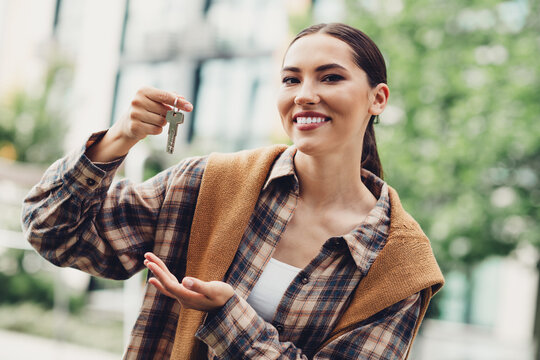 Young woman holding keys outdoors, symbolizing house ownership or rental in a joyful urban outdoor setting