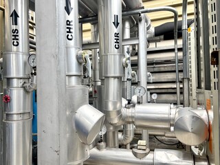 pipes and valves. A close-up view of a complex industrial pipeline system, with blue and silver pipes, red valves, and a pressure gauge, set against a corrugated metal wall.