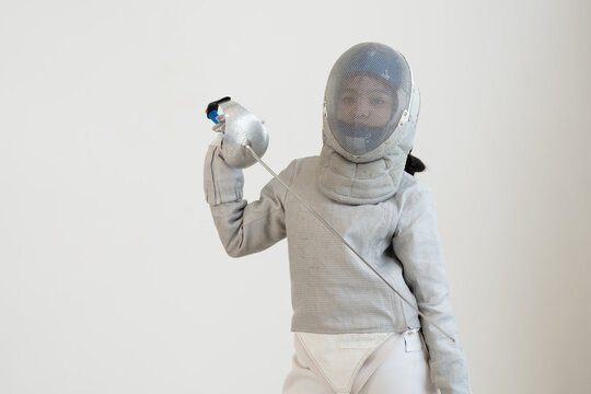 Asian girl in fencing costume with fencing sports mask and holding sword for practicing and training in gym. Teen girl fencer athlete fencing training in classroom