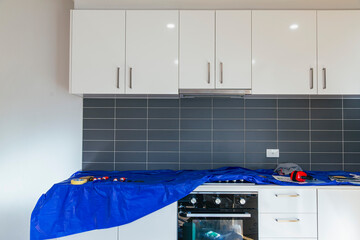 Kitchen renovation in progress with tools and protective blue cover on countertop, glossy cabinets above and tiled backsplash wall