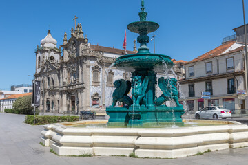 Fototapeta premium View of the Lions Fountain in Porto's square, with water flowing and the twin churches in the background on a calm, sunny day.