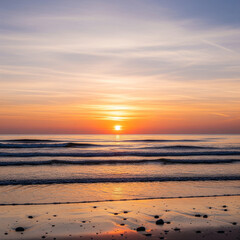 Fototapeta premium A serene sunset over the ocean, with gentle waves lapping at a sandy beach reflecting the warm colors of the sky.