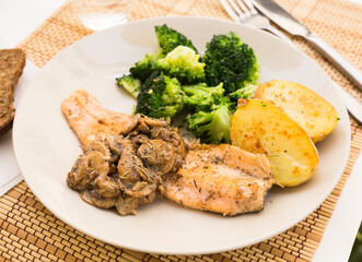 fried river trout fillet with a complex side dish of broccoli, baked potatoes and mushroom sauce