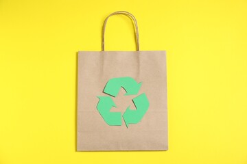 Eco friendly packaging. Recycling symbol and paper bag on yellow background, top view