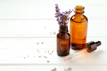 Lavender essential oil and flowers on white wooden table, closeup. Space for text