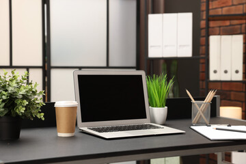 Laptop, takeaway paper cup, houseplants and stationery on black table at home
