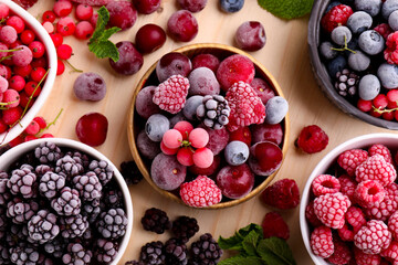 Different ripe frozen berries and mint leaves on light wooden table, flat lay