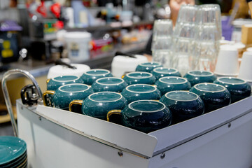 Box of dark green mugs with decorative glaze finish, arranged in rows on retail store shelf with...
