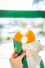 Glazed donut held in hand with bright sunlight and soft focus urban background highlighting sweet treat and casual snack enjoyment