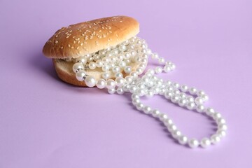 Burger with pearl necklace on lilac background, closeup