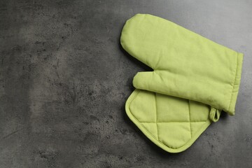 Green oven glove and potholder on dark textured table, top view. Space for text