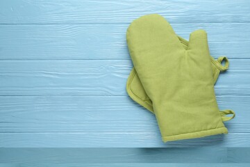Green oven glove and potholder on light blue wooden table, top view. Space for text