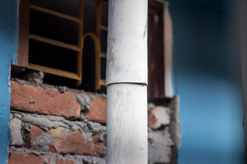 Closeup of a white pipe against a brick wall and window
