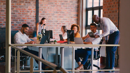 Business Team At Desks Working Together In Busy Multi-Cultural Office