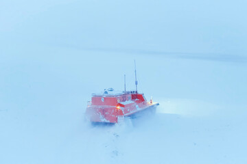 Orange swamp vehicle on caterpillars driving through winter tundra oil field