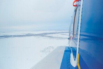 View from the helicopter on snow-covered tundra. A helicopter is partially visible