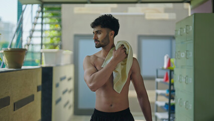 Indian young adult man guy walking indoor changing room hold towel wipe off sweat after morning fitness workout Asian relax sports male well being boy take break time at inside campus