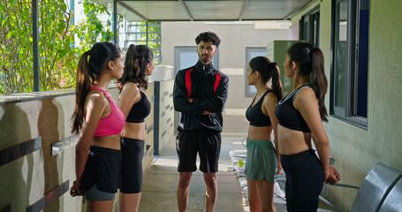 Obraz premium Indian young adult gen z sports woman lady group team fit coach man talk speak share plan ideas day time at campus place male guy explain game to female girls player in break time indoor area