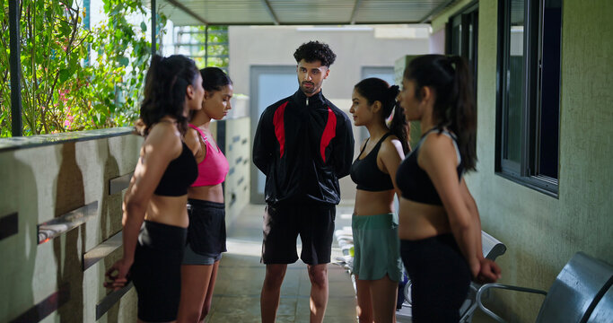 Indian young adult gen z sports woman lady group team fit coach man talk speak share plan ideas day time at campus place male guy explain game to female girls player in break time indoor area