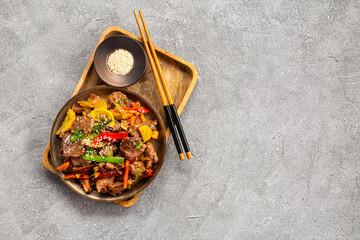 Beef stir fry in a plate top view, Asian meat with vegetables on a grey background copy space for text