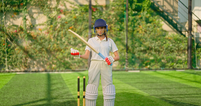 Indian gen z athlete sports woman lady standing staring cam play ground wear white uniform and protective helmet look camera. Asian cricket player female girl hold bat day time at match