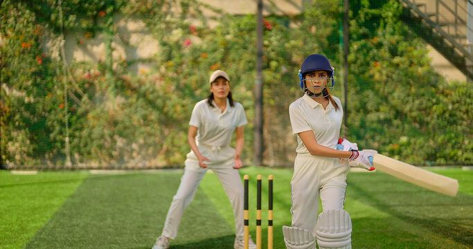 Indian gen z young adult sports woman lady wear hand gloves white dress leg guard helmet day time cricket player teen female girl hold bat play casual match game do batting at ground place - Powered by Adobe