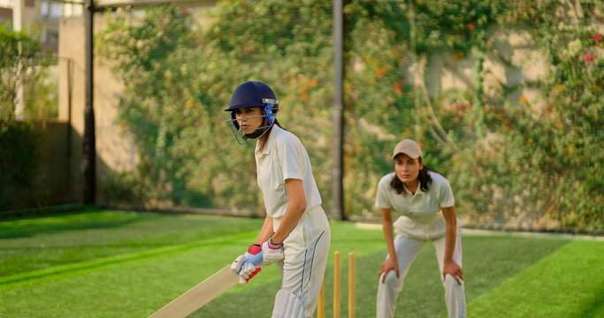 Indian gen z young adult sports woman girl standing at outdoor match play ground wear gloves white uniform and protective helmet Asian athlete cricket player female lady hold bat do practice day time