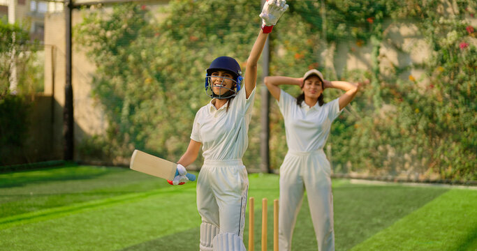 Indian gen z young adult woman lady wear hand gloves white dress leg guard helmet day time cricket player sports teen female girl hold bat play casual match game hit ball do batting at ground place - Powered by Adobe