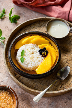 Thai mango sticky rice with coconut milk, garnished with edible flowers on light background vertical photo