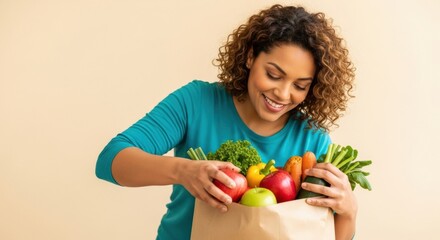 Fototapeta premium A happy African American woman looks into her paper grocery bag filled with fresh, healthy fruits and vegetables from the market.