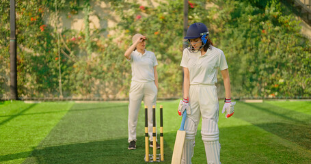 Indian gen z young adult sports woman lady wear hand gloves white dress leg guard helmet day time cricket player teen female girl hold bat play casual match game do batting at ground place
