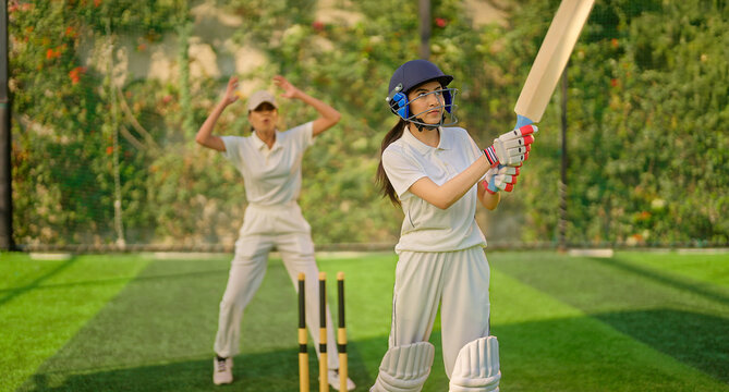 Indian gen z young adult sports woman lady wear hand gloves white dress leg guard helmet day time cricket player teen female girl hold bat play casual match game do batting at ground place - Powered by Adobe