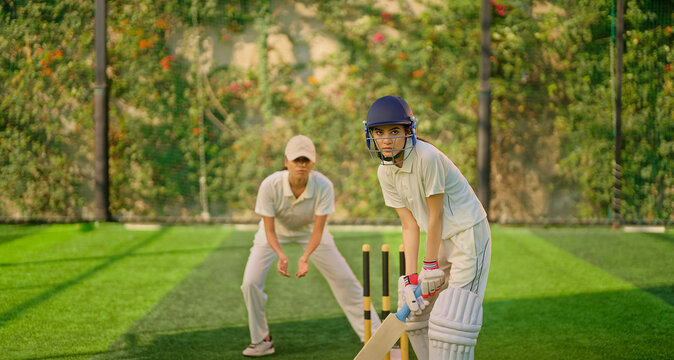 Indian gen z young adult sports woman lady wear hand gloves white dress leg guard helmet day time cricket player teen female girl hold bat play casual match game do batting at ground place