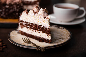 A piece of tiramisu cake with chocolate and whipped cream on dark background