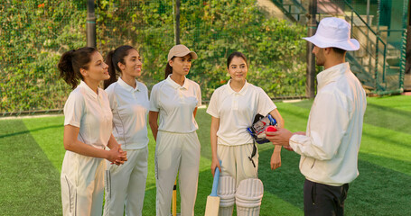 Indian asian young adult gen z woman lady group team standing coach man do sports discussion at match male guy trainer explain game strategy girls female player wear white uniform outdoor play ground