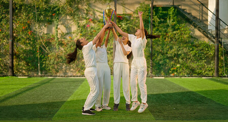 Indian young adult gen z sports woman lady group win match held award in hand raise up enjoy day time happy female team cheering have fun joy do jump shout loud scream yes at play ground place