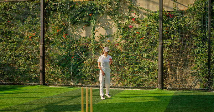 Indian young adult gen z bowler woman lady standing at match ground wear white uniform with cap. Asian teen age female girl running play cricket learn game do practice to hit wicket throw ball place - Powered by Adobe