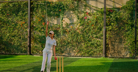 Indian young adult gen z bowler woman lady standing at match ground wear white uniform with cap. Asian teen age female girl running play cricket learn game do practice to hit wicket throw ball place