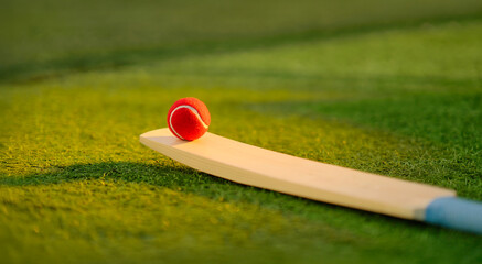 close up of red ball and cricket bat lying on green grass outdoor ground place