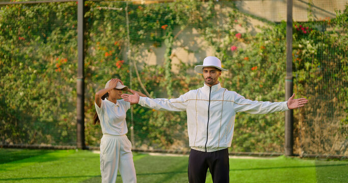 Indian Asian young adult gen z bowler woman outdoor match play ground wear white uniform cap female lady girl skill do practice hit wicket stump umpire man show no ball with wide hand sign day time