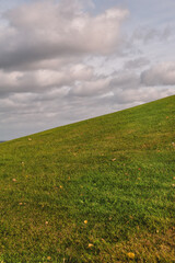 Fototapeta premium Green grassy hill under cloudy sky creates peaceful natural scenery