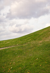 Green grassy hill under cloudy sky creates peaceful natural scenery