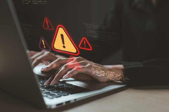 Hands typing on laptop with warning signs and code overlay, representing cybersecurity threats, system error, malware attack, data breach, or hacking alert in digital environment.
