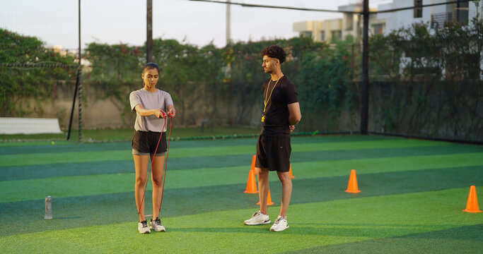 Indian young adult gen z woman lady jump on skip rope work out for weight lose. fit man gym trainer male guy coach watch sports female girl do daily health care learn good habit game garden place area - Powered by Adobe