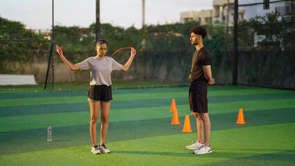 Indian young adult gen z woman lady jump on skip rope work out for weight lose. fit man gym trainer male guy coach watch sports female girl do daily health care learn good habit game garden place area