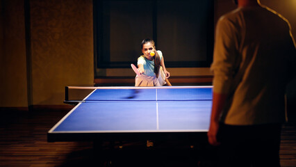 Indian happy young adult gen z athlete player woman hold racket play table tennis male man passing ball indoor dark room Asian sporty girl lady do sports training enjoy ping pong game have fun joy	