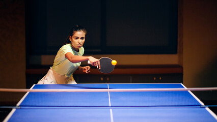 Indian asian young adult gen z athlete player woman hold racket play table tennis passing ball indoor dark room sporty girl lady do sports training enjoy ping pong game have fun joy  © Raushan_films